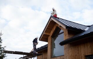 Roofing workers installing metal roofing on a modern wooden house.