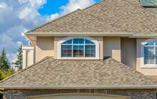 Close-up of a house's upper story with two large arched windows and a shingled roof.
