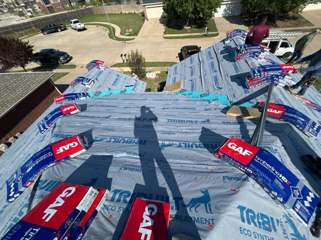Roof under construction with GAF roofing materials and workers installing new shingles.