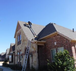 Roofing worker on ladder installing or inspecting roof shingles on a residential house.