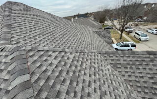 View of a gray shingled roof with neighboring houses and trees in the background.