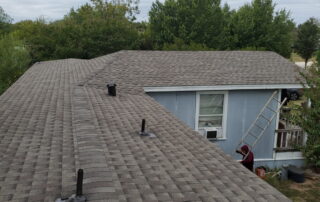 Roofing work in progress on a blue house with a ladder and workers installing gutters.
