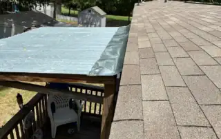 Roof with new shingles and a section with a protective tarp for gutter installation.