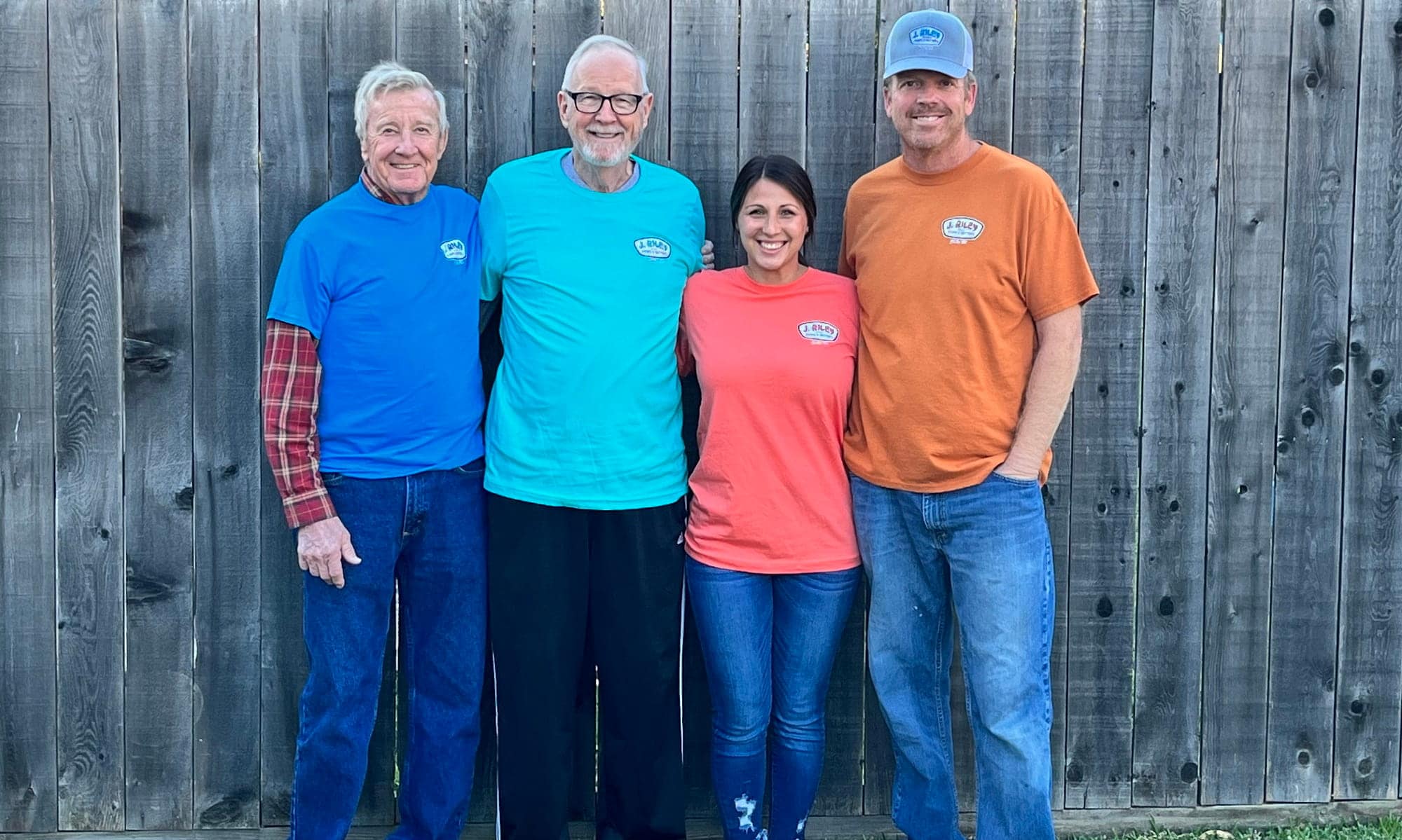 Four J. Riley Roofing & Gutters team members standing in front of a wooden fence.