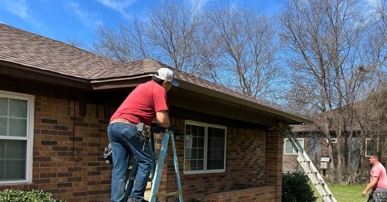 Worker installing gutter guards on a residential house in a suburban neighborhood.