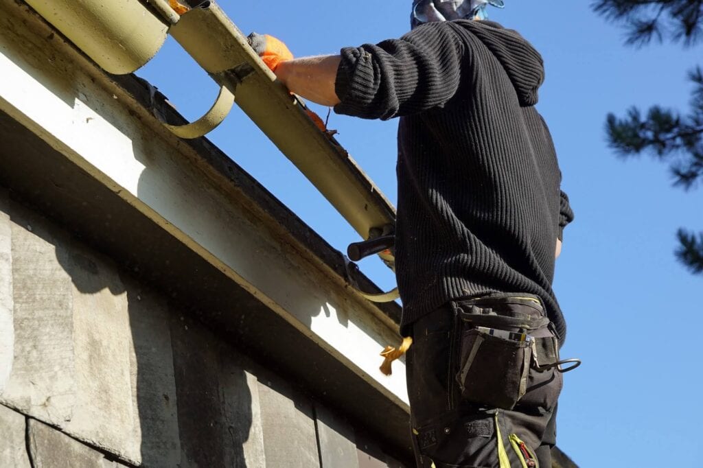 Worker installing gutter guard on residential roof in daylight.